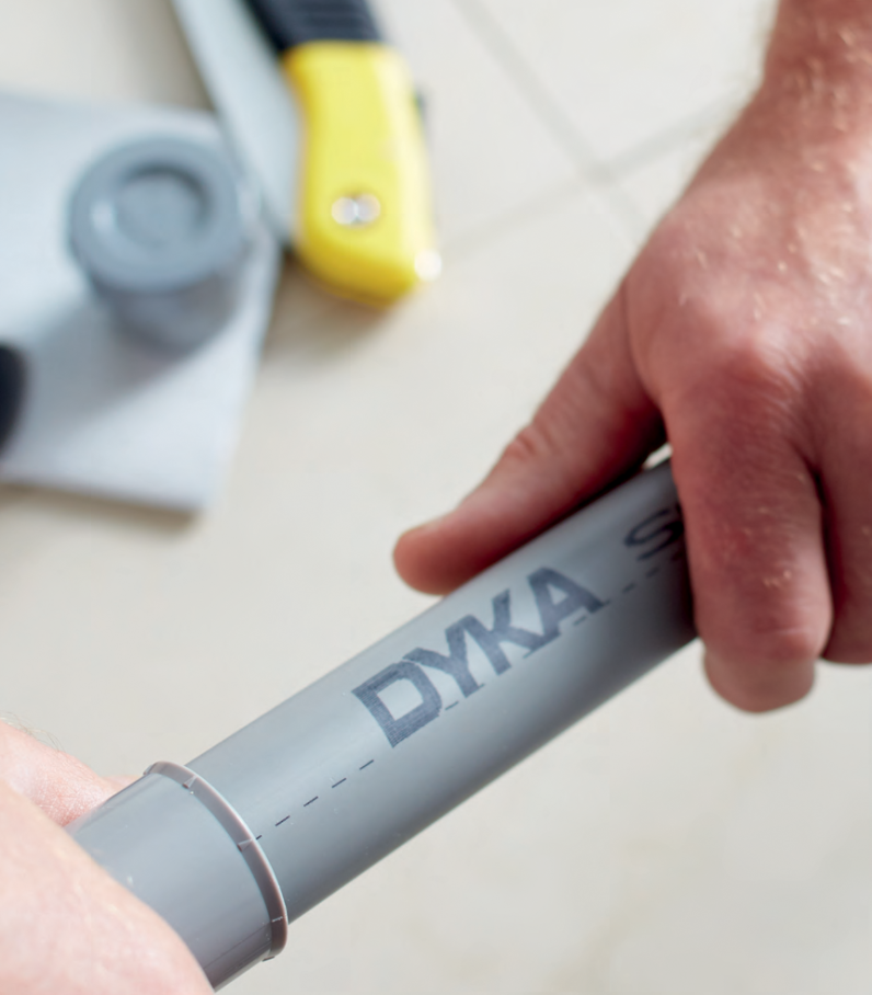 Présentation du système DYKA fast avec un plombier emboitant un tube en PVC gris avec un raccord. Le tube est marqué d'une ligne et le raccord de marquer d'emboiture tous les 45 degrès